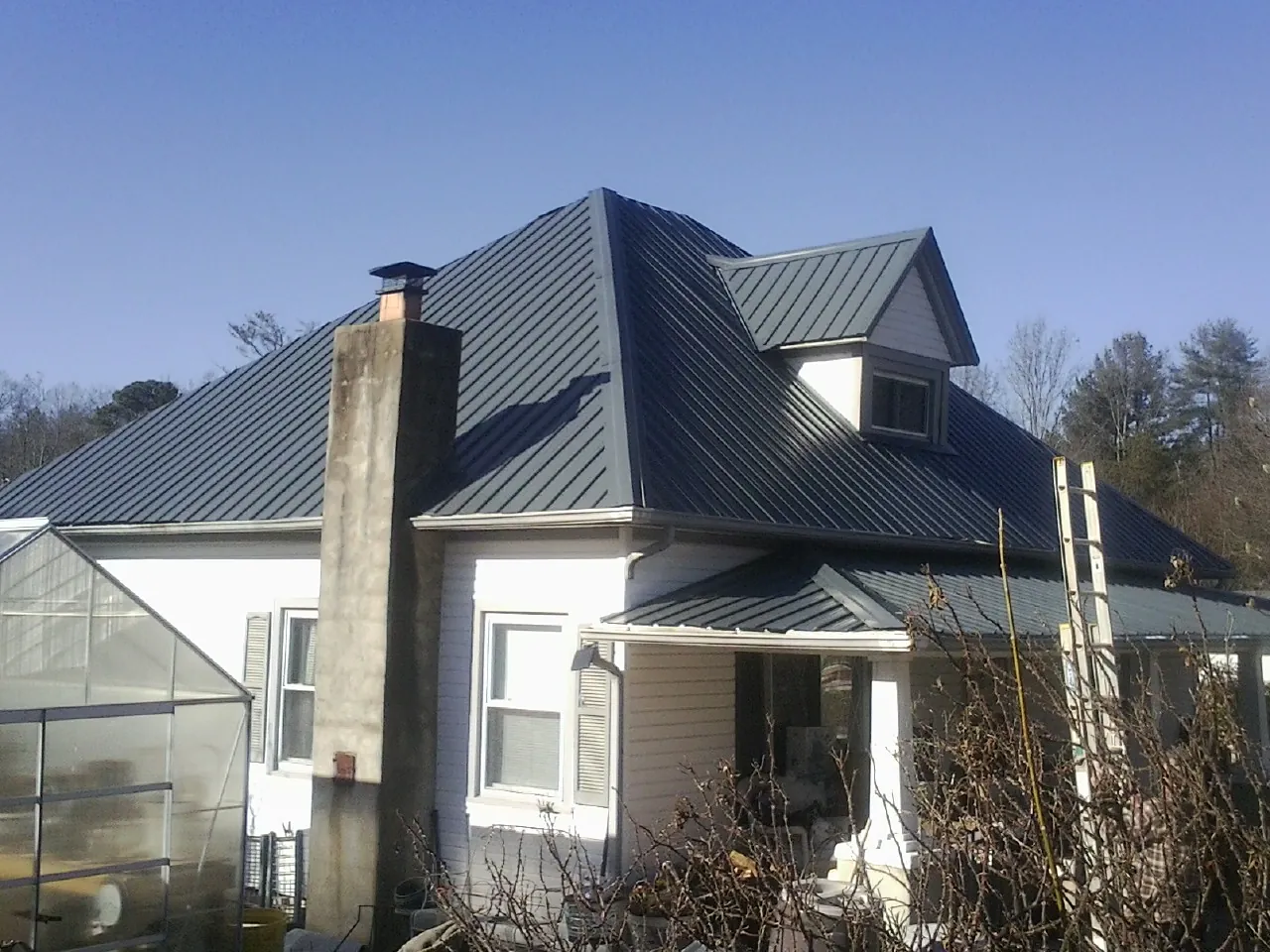 Dark blue standing seam metal roof on a white farmhouse with dormer — Slate & Tile Roof Repair by Roofing Brothers in Abie