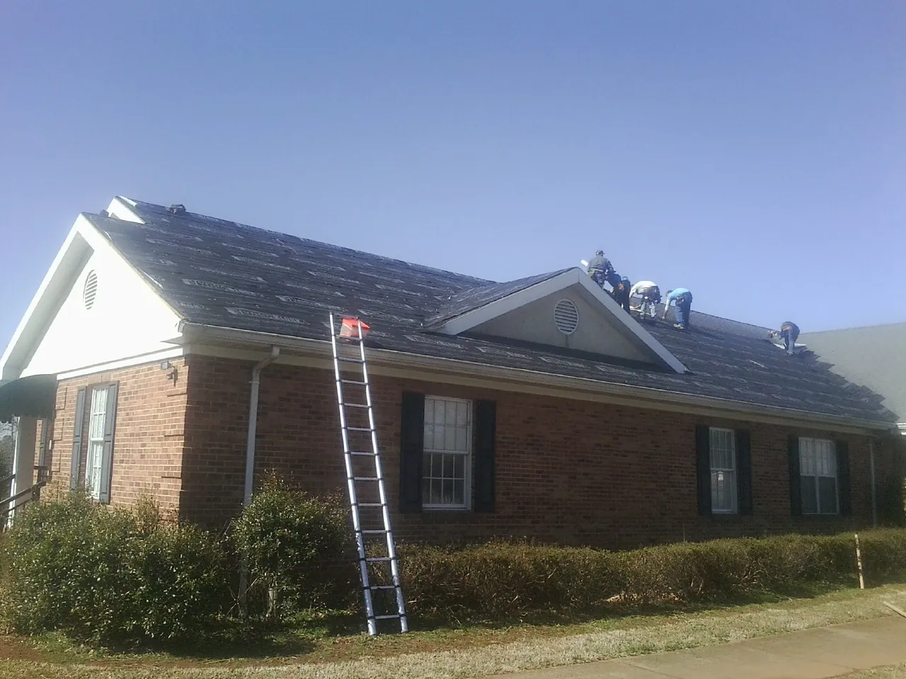 Crew tearing shingles off a brick ranch roof with a ladder set — Metal Roof Repair work by our crew in Abie