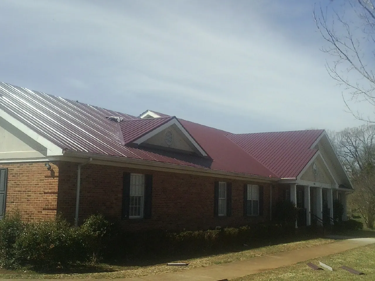 Red metal roof with gabled entries on a long brick building, from a Hail Damage Roof Repair job in Abie