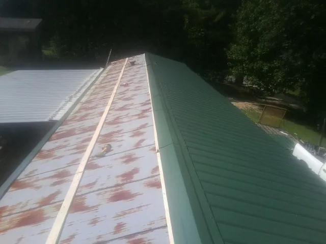 Old rusted panels beside newly installed green metal roofing — Wind Damage Roof Repair by Roofing Brothers in Abie