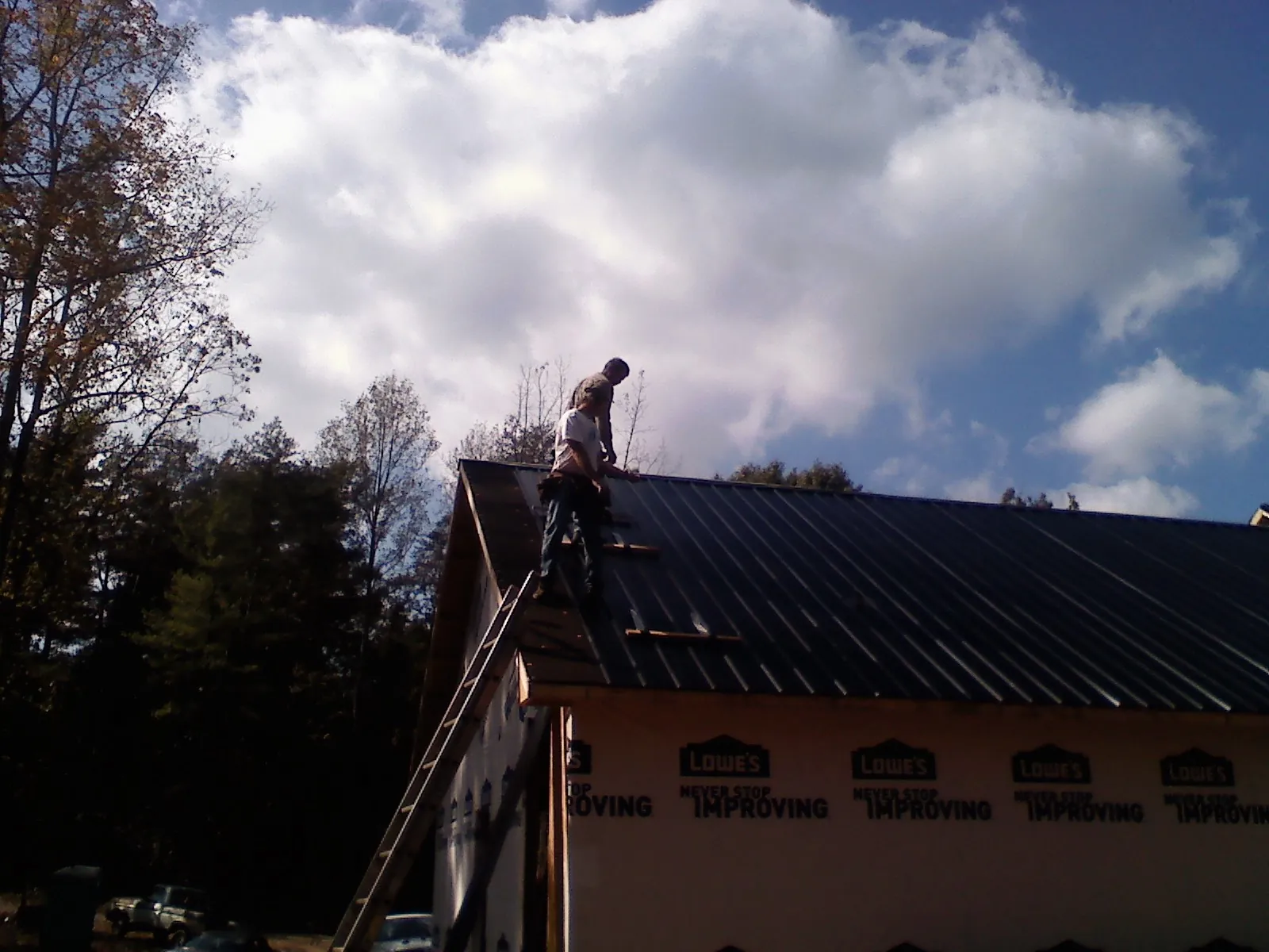 Roofer fastening dark metal panels high against a cloudy sky, from a Roof Inspection job in Abie
