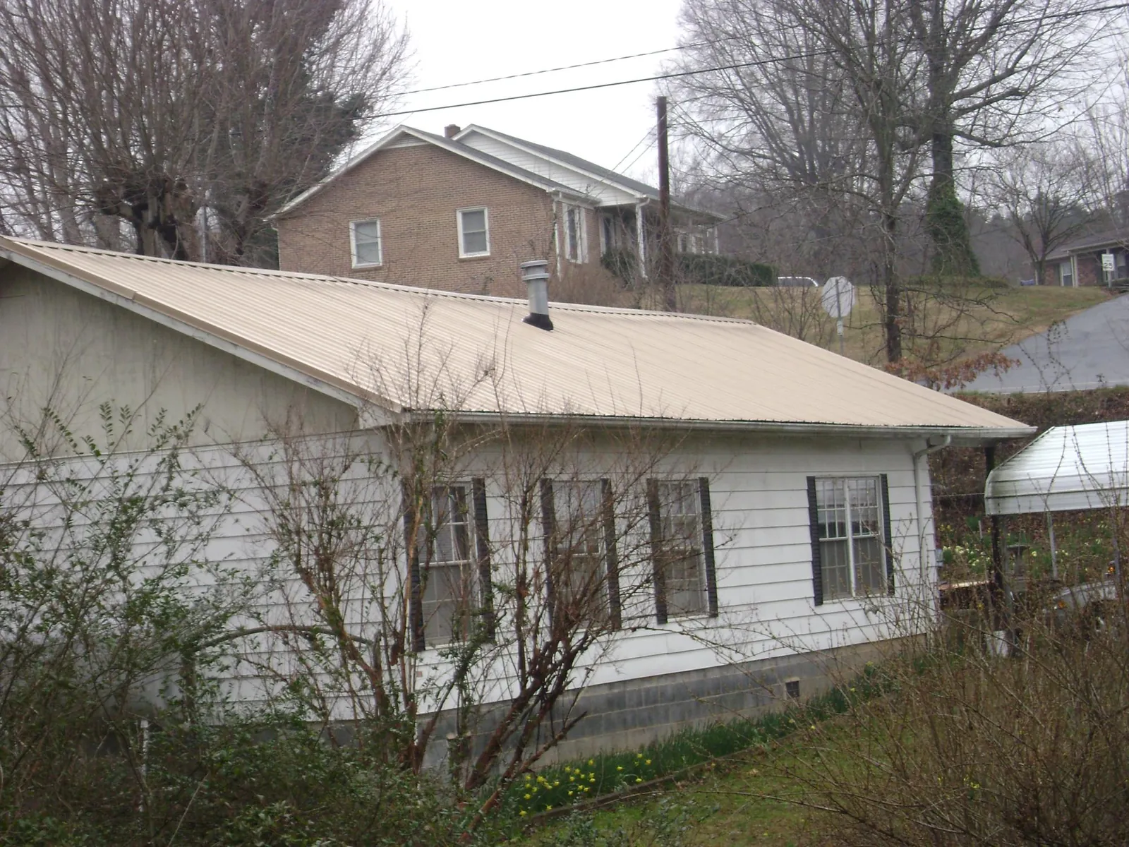 Tan metal roof on a white sided house set into a hillside — Commercial Roofing by Roofing Brothers in Abie