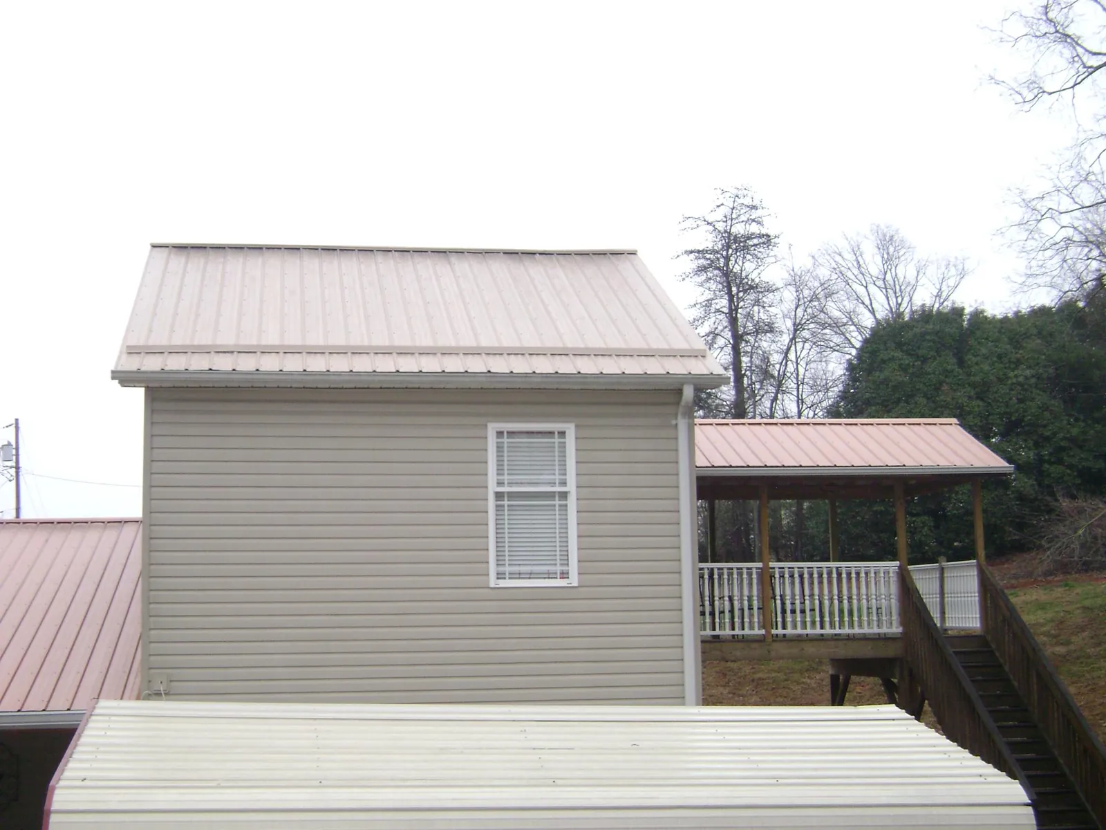 Tan metal roofs on a two story addition and attached porch, from a Roof Replacement job in Abie